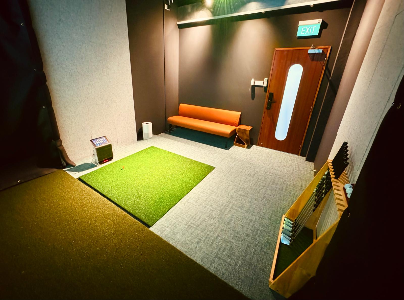 Inside a private indoor golf simulator bay — putting turf, screen, and clubs ready